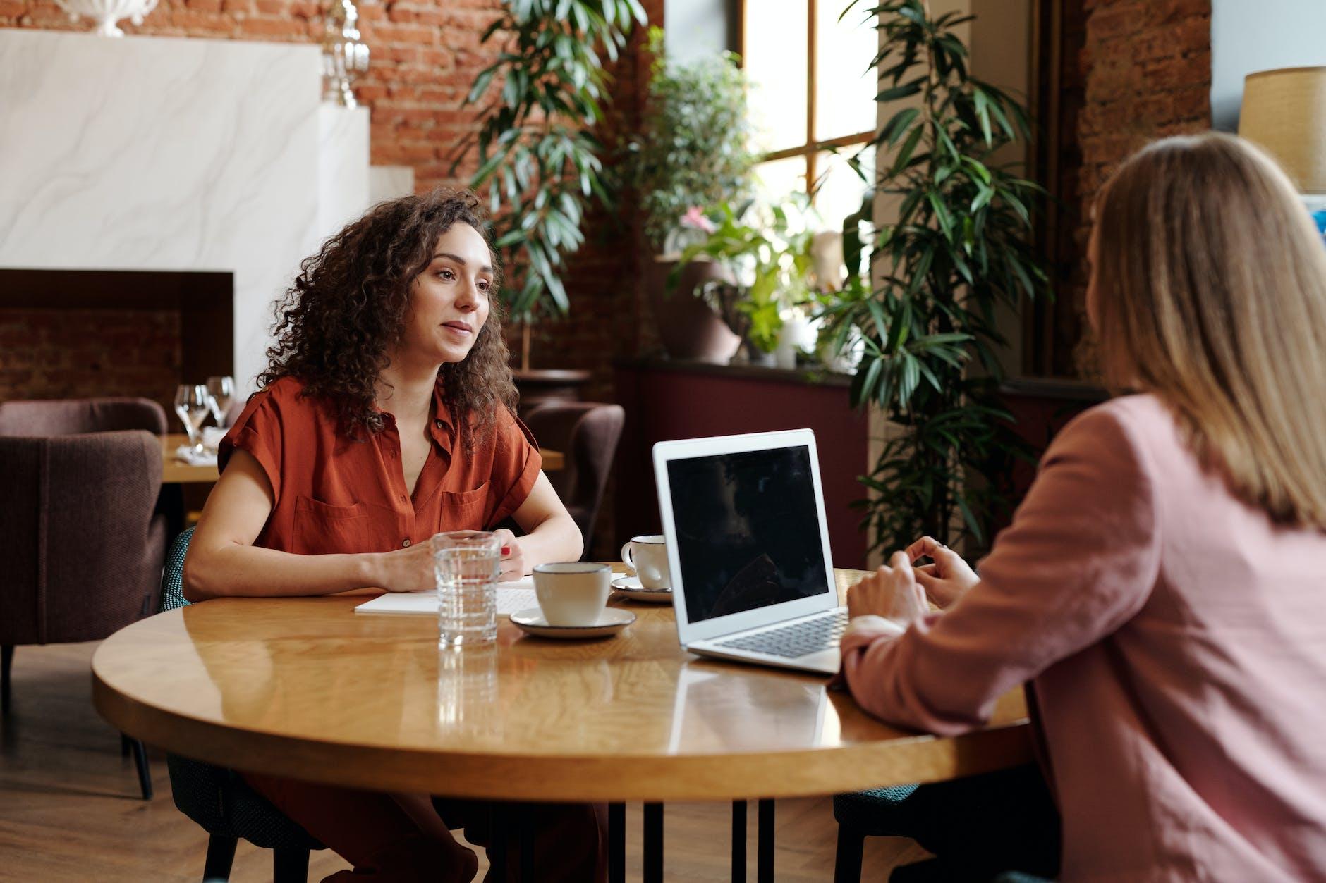 women sitting on table with cups of coffee and laptop